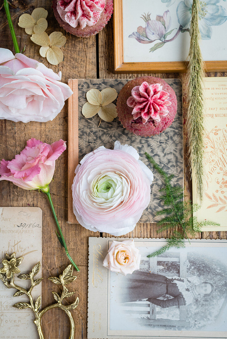 Pink flowers, vintage cards, antique photos and strawberry cupcakes on wooden table