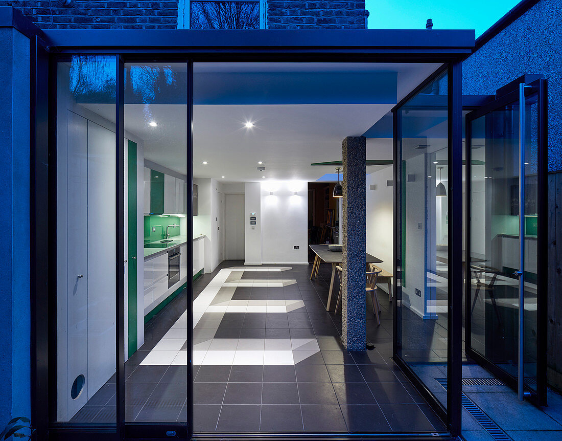 Blick durch offene Glasfront in die moderne Wohnküche am Abend
