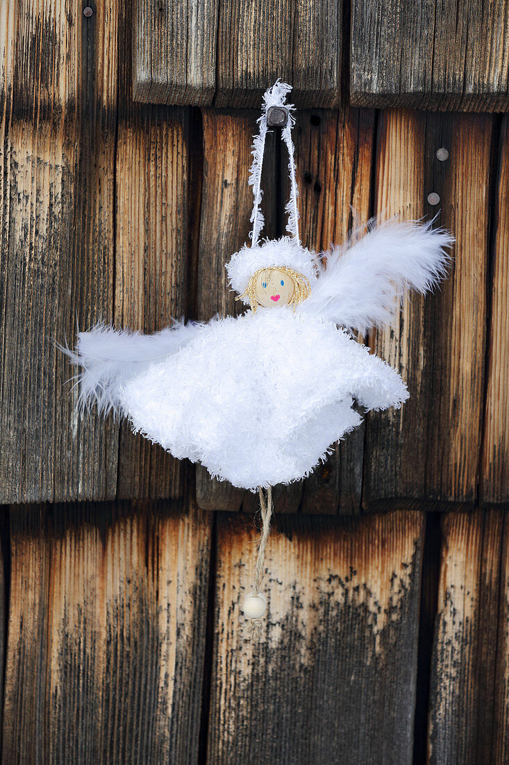 DIY-Engel mit weißen Kleidchen vor Holzwand