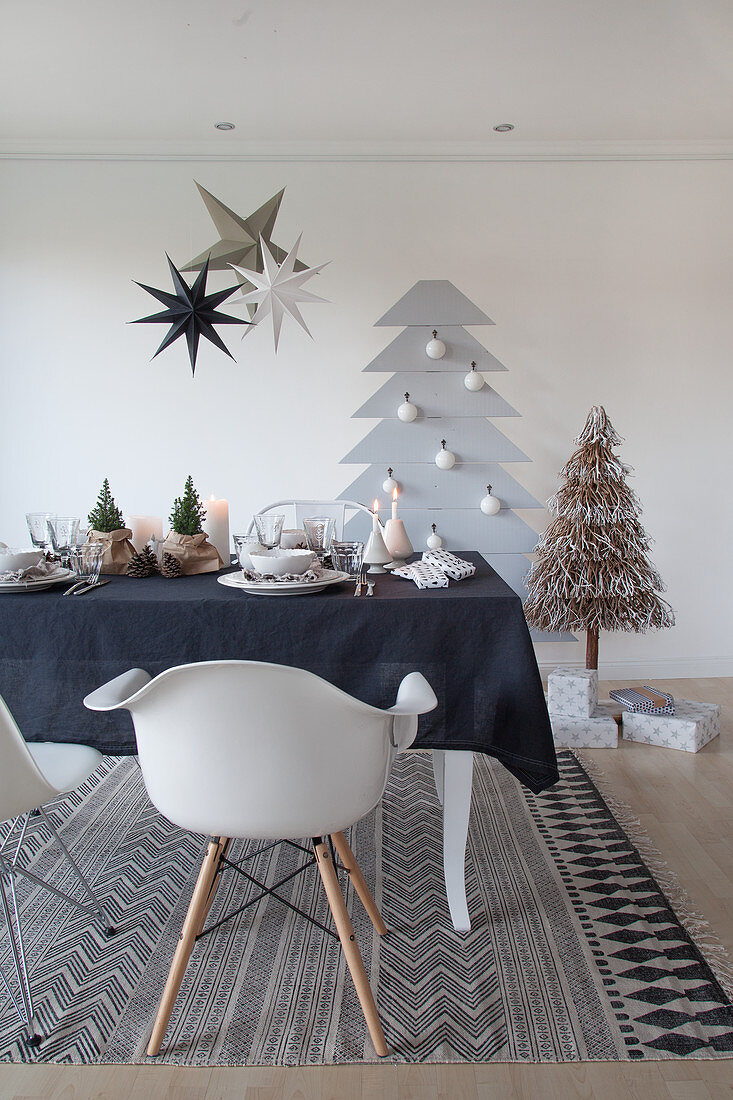 Gedeckter Weihnachtstisch mit schwarzer Tischdecke, stilisierter Weihnachtsbaum an der Wand