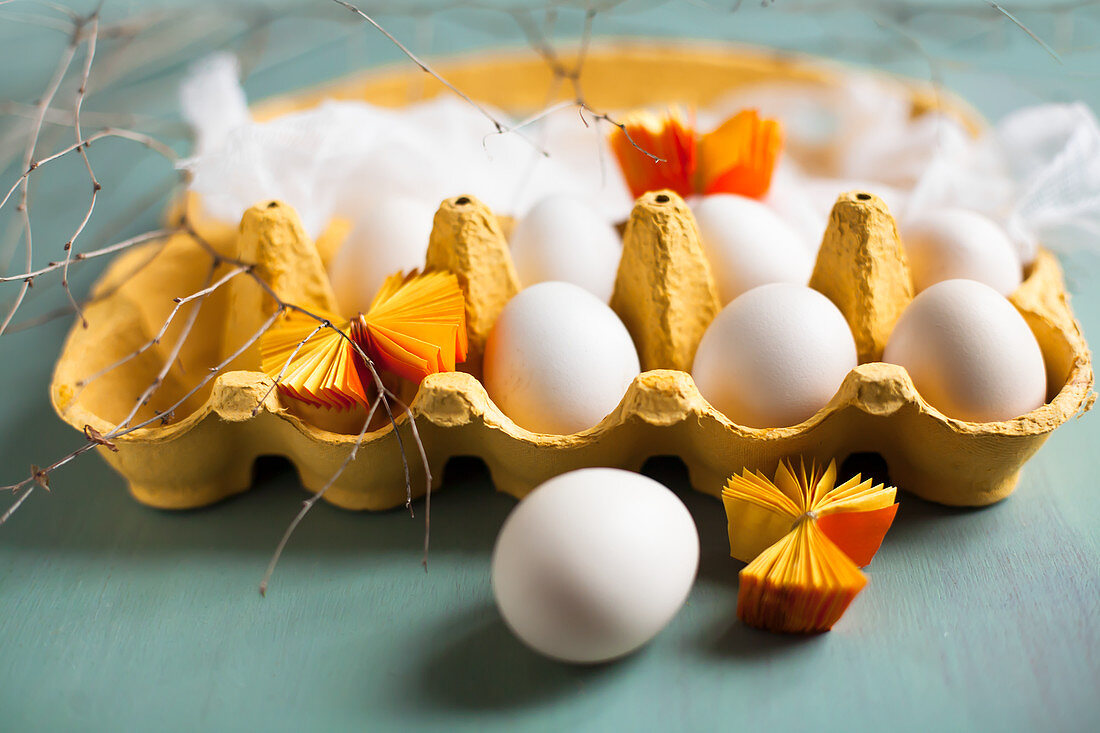 weiße Eier, Mulltuch und gelbe Papierrosetten in gelbem Eierkarton