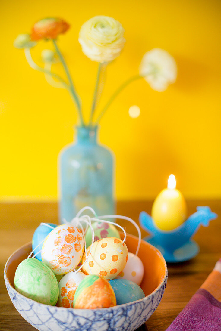 Mit Gouache-Farben bemalte Ostereier vor Kerze und Blumen