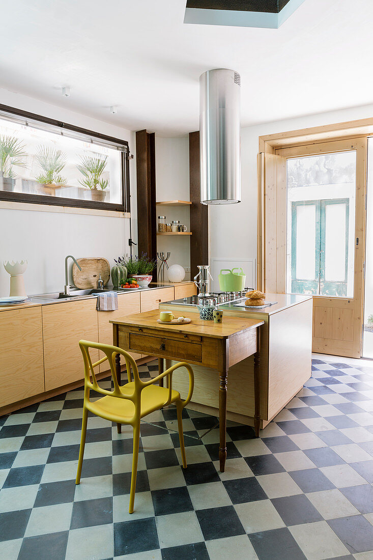 Kücheninsel, Küchentisch und gelber Stuhl auf Schachbrettmusterboden in Wohnküche mit Terrassentür