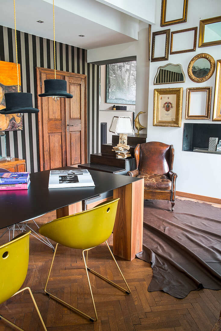 Gelbe Schalenstühle um Tisch mit schwarzer Tischplatte und Massivholz Beinen, verschiedene Bilderrahmen an der Wand