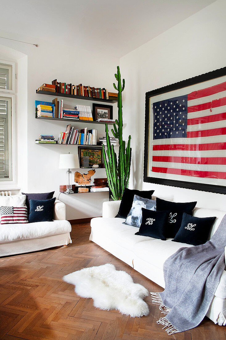 weiße Sofagarnitur mit Kissen und Plaid, Schaffell, Wandregal, Kaktus und US-Flagge an der Wand