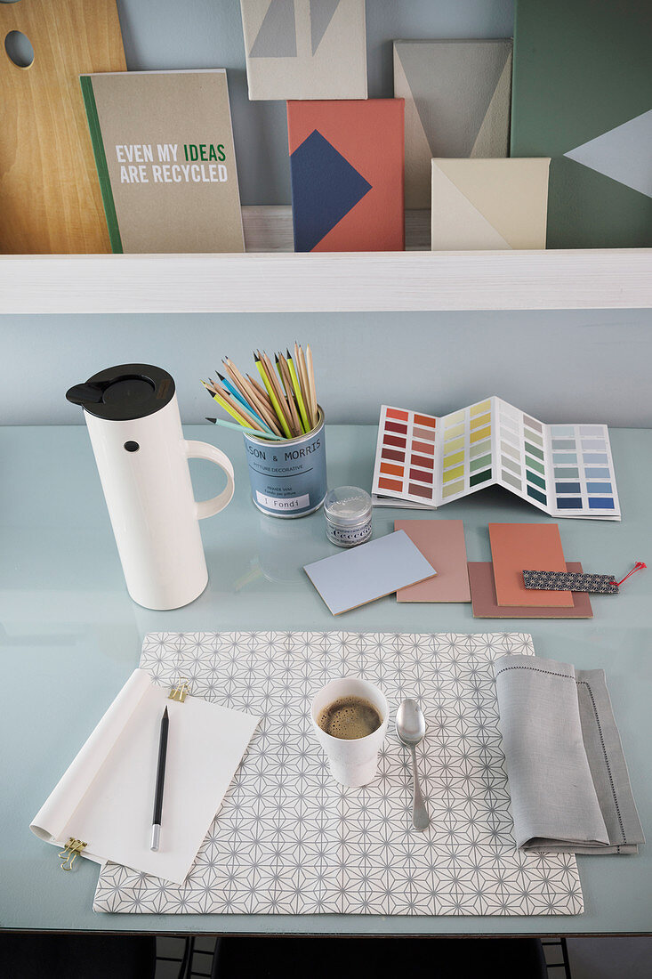 Blick auf Schreibtisch mit Thermoskanne, Kaffee, Schreibutensilien und Farbpalette