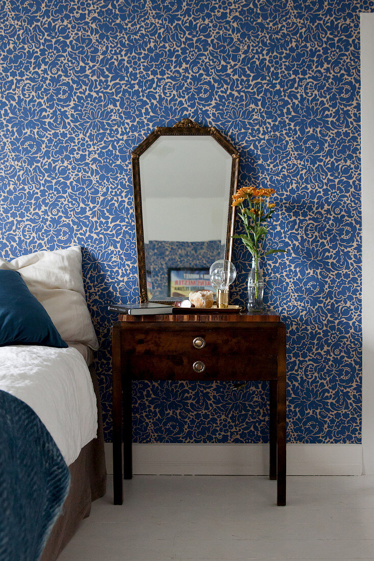 Old mirror and bedside table against blue floral wallpaper