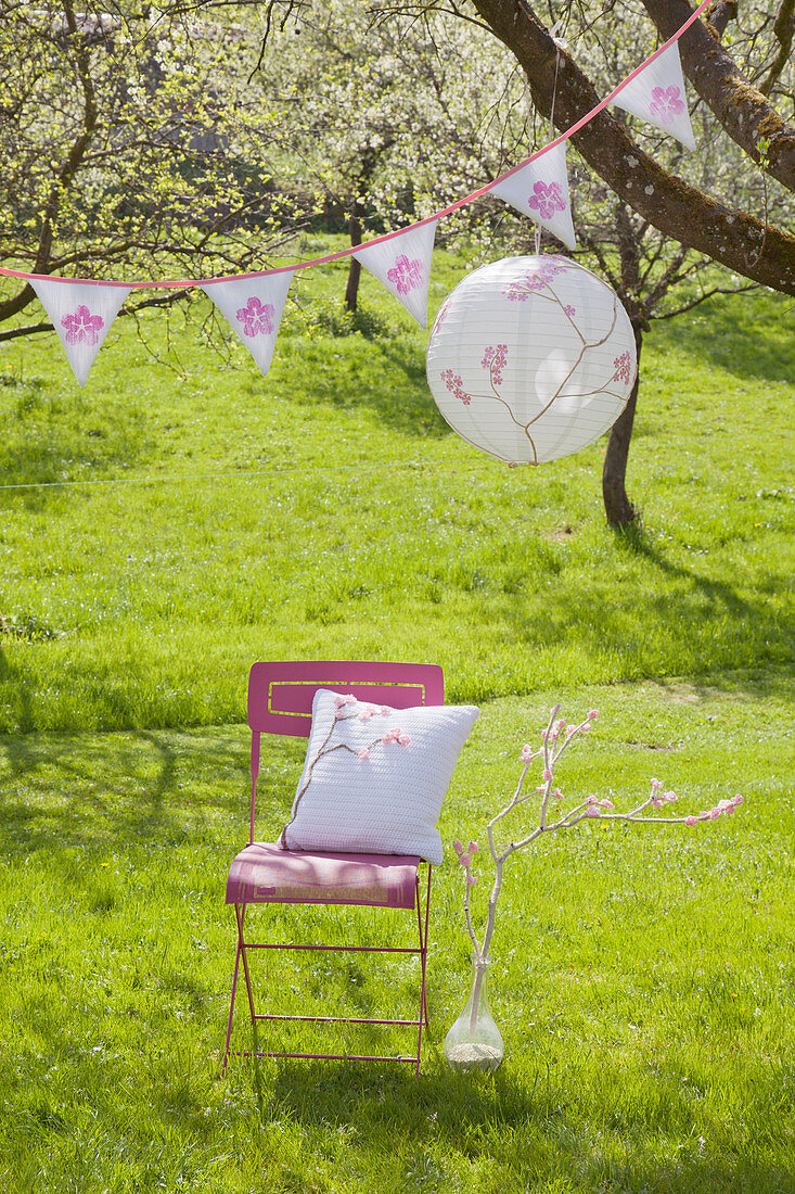 Romantischer Platz unter blühendem Kirschbaum mit Lampion und Wimpelkette: DIY-Kissen auf Stuhl, daneben umwickelter Ast mit Häkelblüten