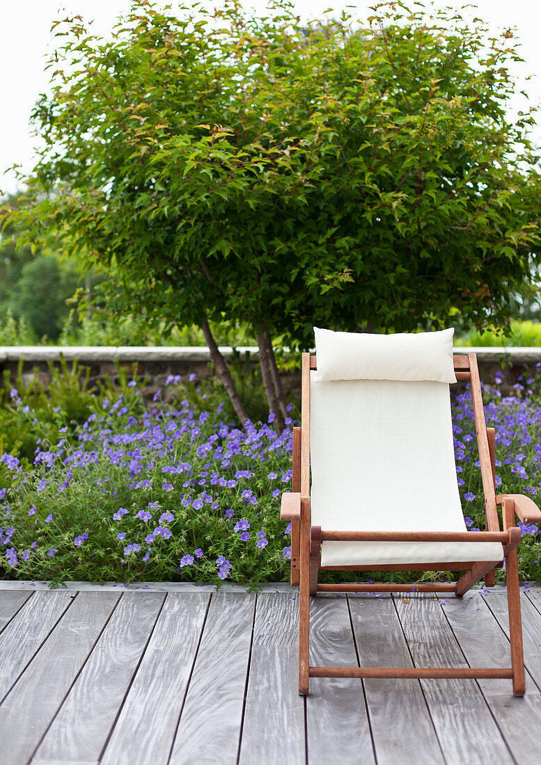 Liegestuhl auf der Terrasse vor Beet mit Storchschnäbeln und Bäumchen