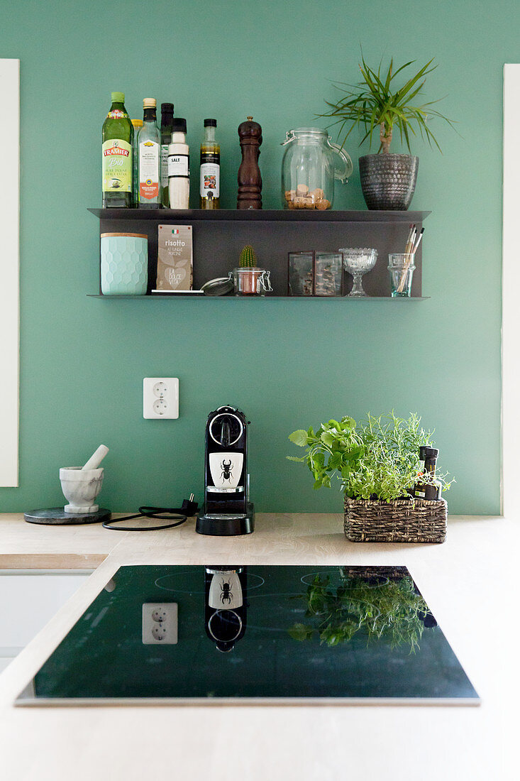Black shelf mounted on petrol-blue kitchen wall above hob