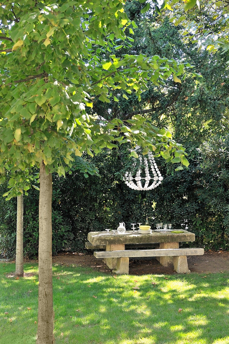 Stone bench and table below chandelier in garden