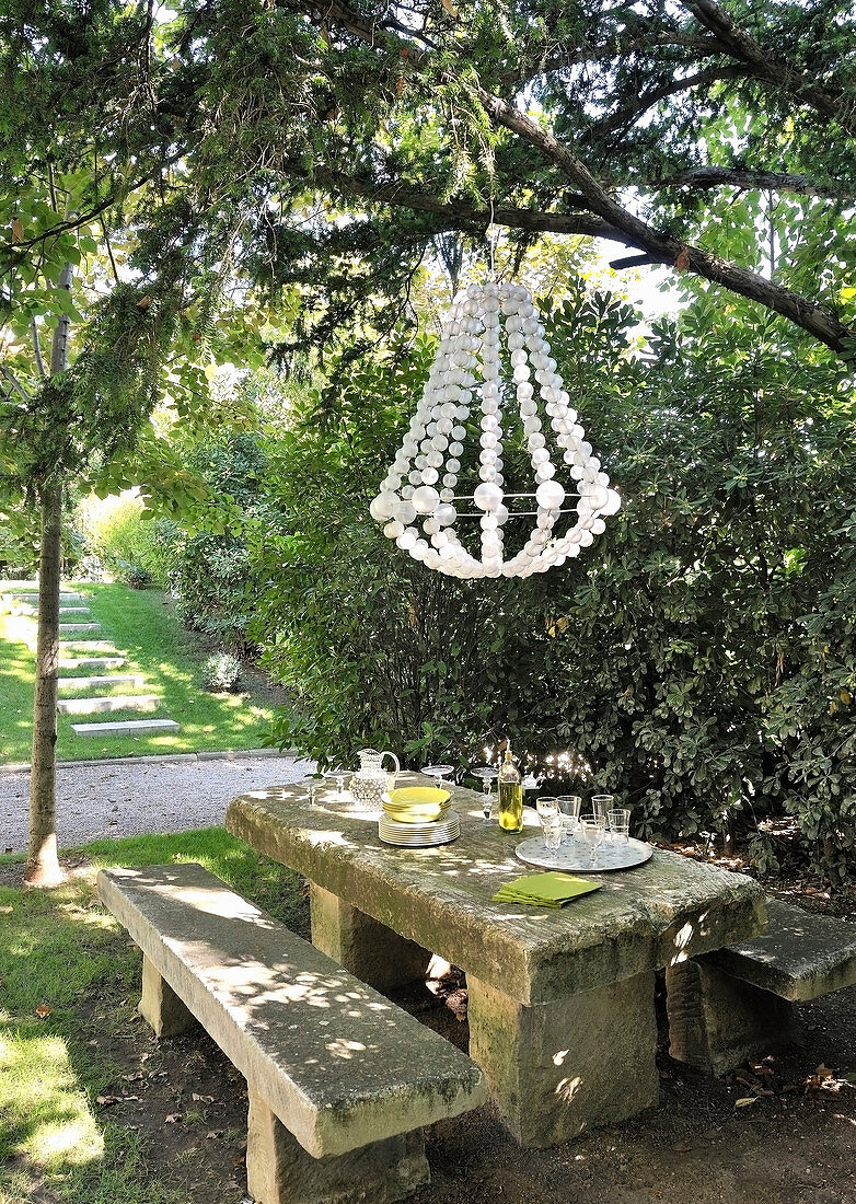 Stone bench and table below chandelier in garden
