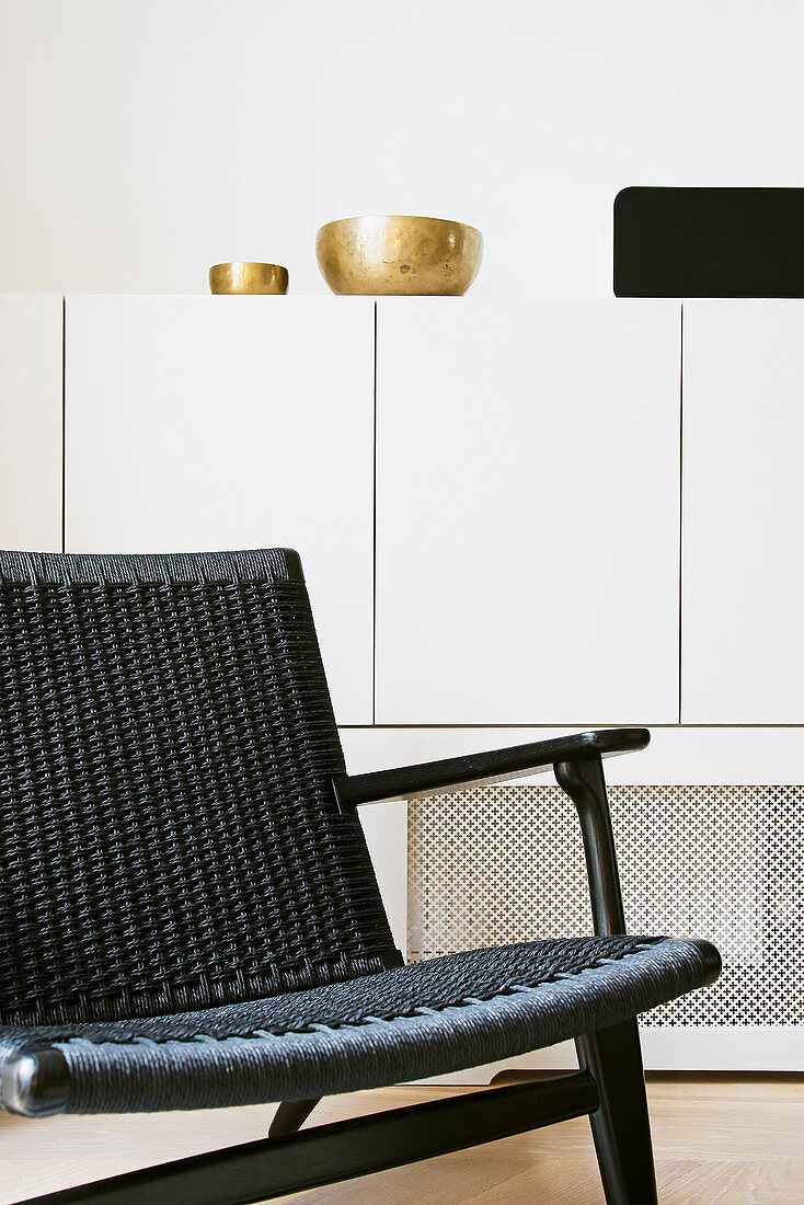 Black chair in front of gold bowls on white sideboard