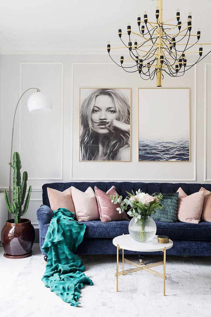 Dunkelblaues Sofa mit Kissen darüber großformatige Fotos in hellem Wohnzimmer