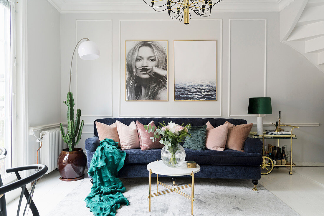 Dunkelblaues Sofa mit Kissen darüber großformatige Fotos in hellem Wohnzimmer