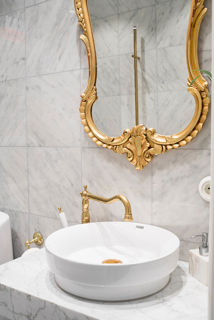Gilt-framed mirror above countertop sink on marble washstand in bathroom