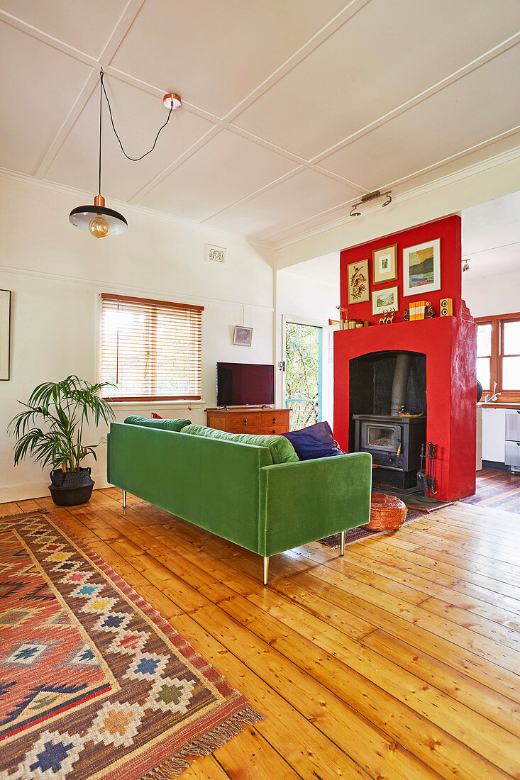 Grünes Sofa und Kaminofen mit roter Wandverkleidung im Wohnzimmer mit Holzdielenboden