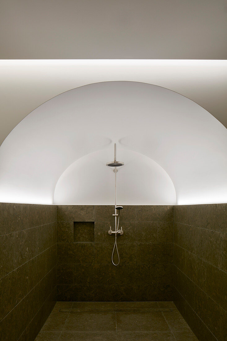 Shower in vaulted room with half-height tiled walls and indirect lighting