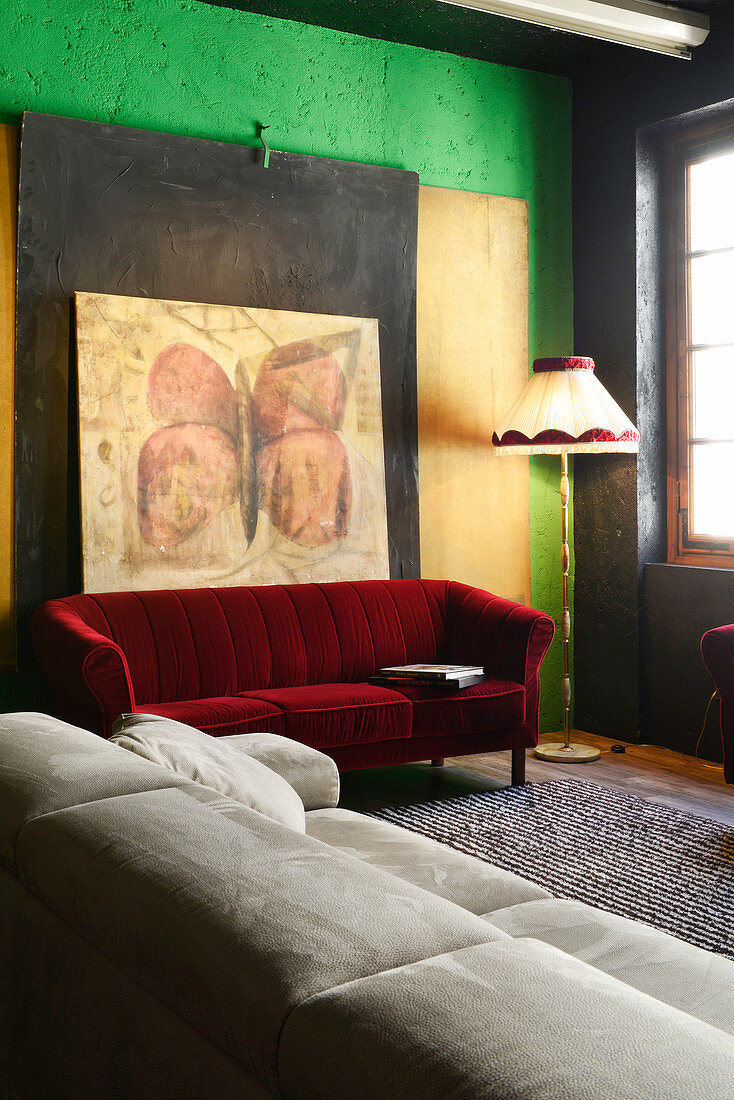 Red velvet sofa below large artwork on wall and pale leather sofa in renovated loft apartment
