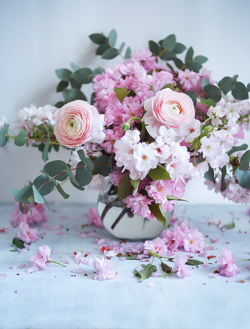 Rosafarbener Blumenstrauß aus Ranunkeln, Kirschblüten und Eukalyptus in einer Vase