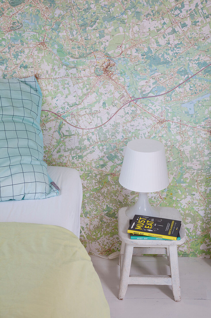 Stool used as bedside table in bedroom with map-patterned wallpaper