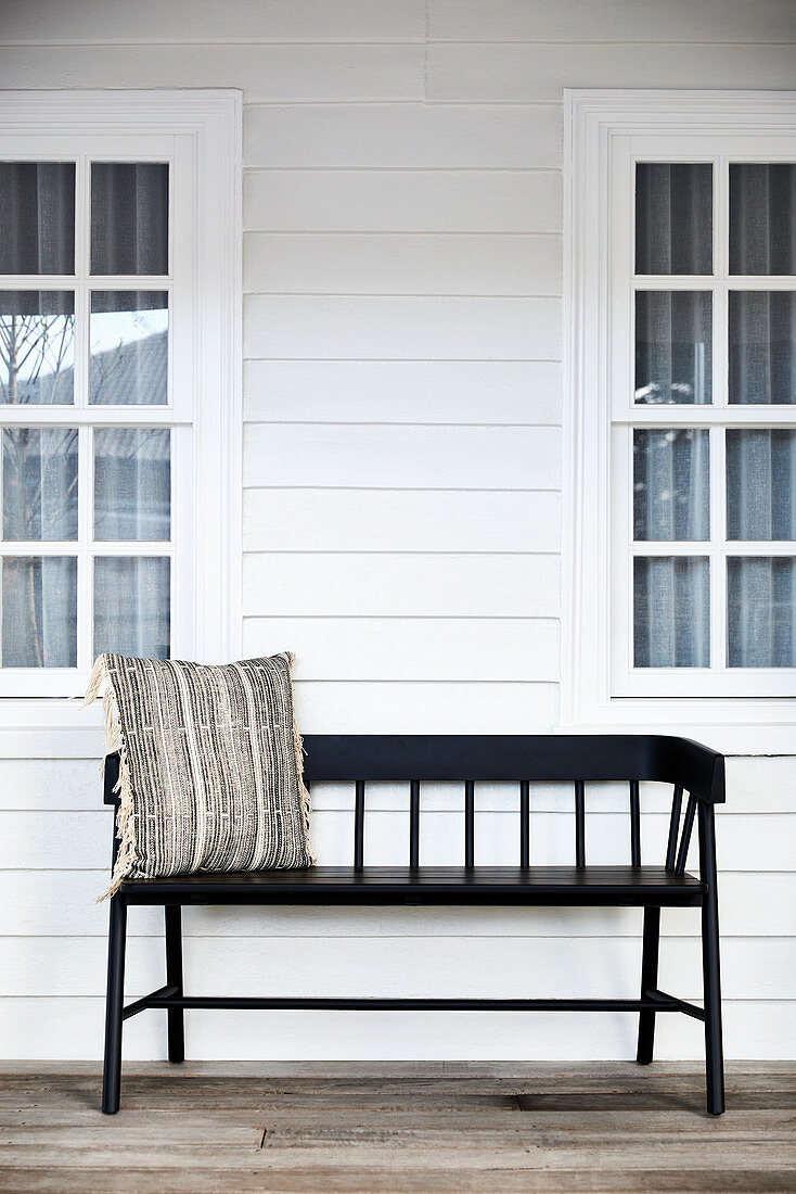 Black wooden bench with scatter cushion outside wooden house