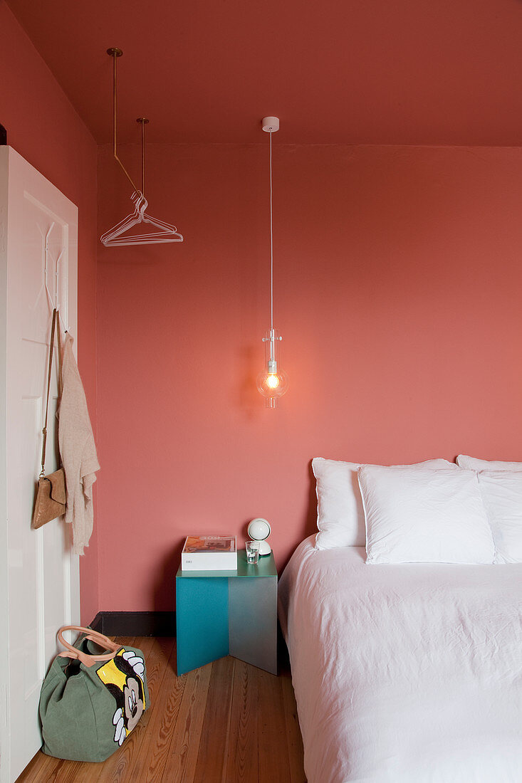 Bed with white bed linen in bedroom with salmon-pink walls