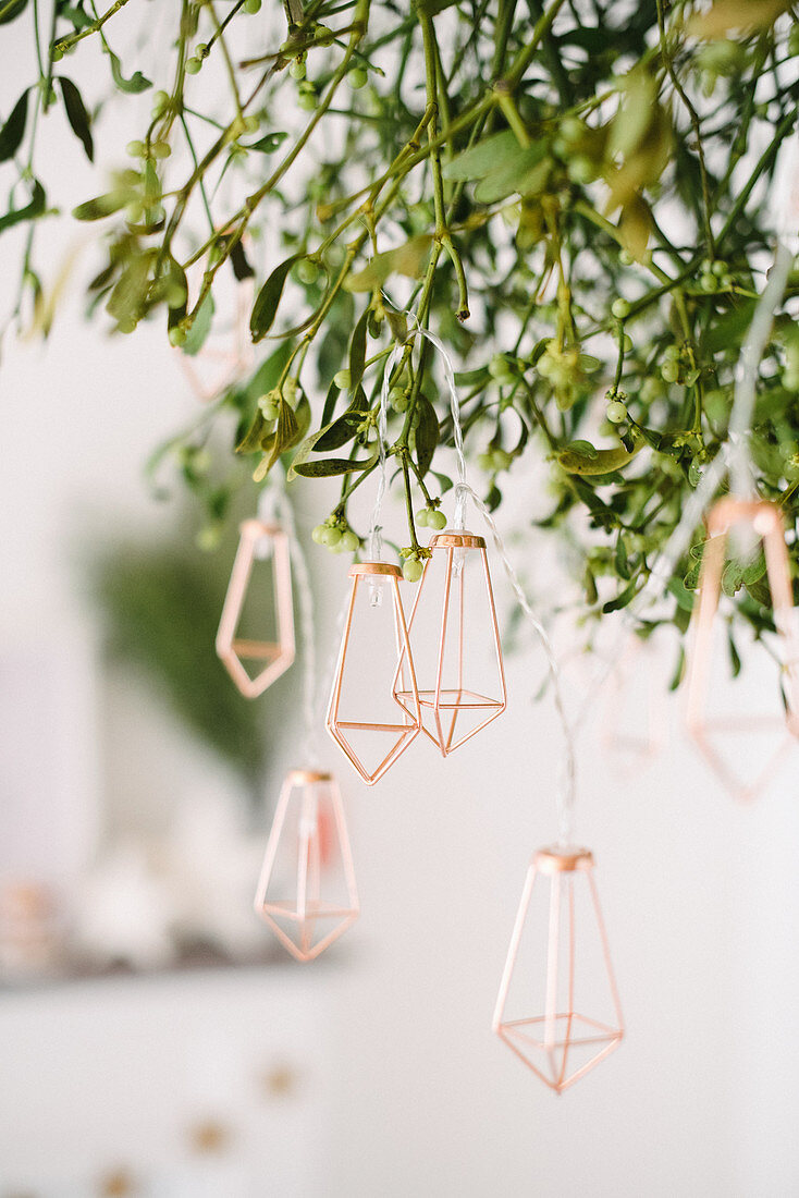 Fairy lights with golden metal ornaments hung from bunch of mistletoe