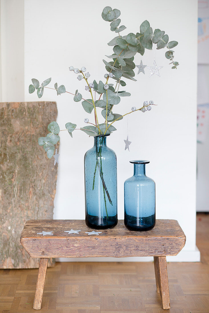 Zwei blaue Vasen mit Eukalyptuszweigen auf einem Schemel