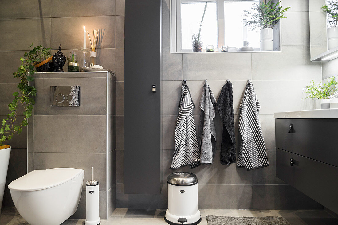 Badezimmer mit grauen Wandfliesen, Blick auf Toilette und Waschtisch