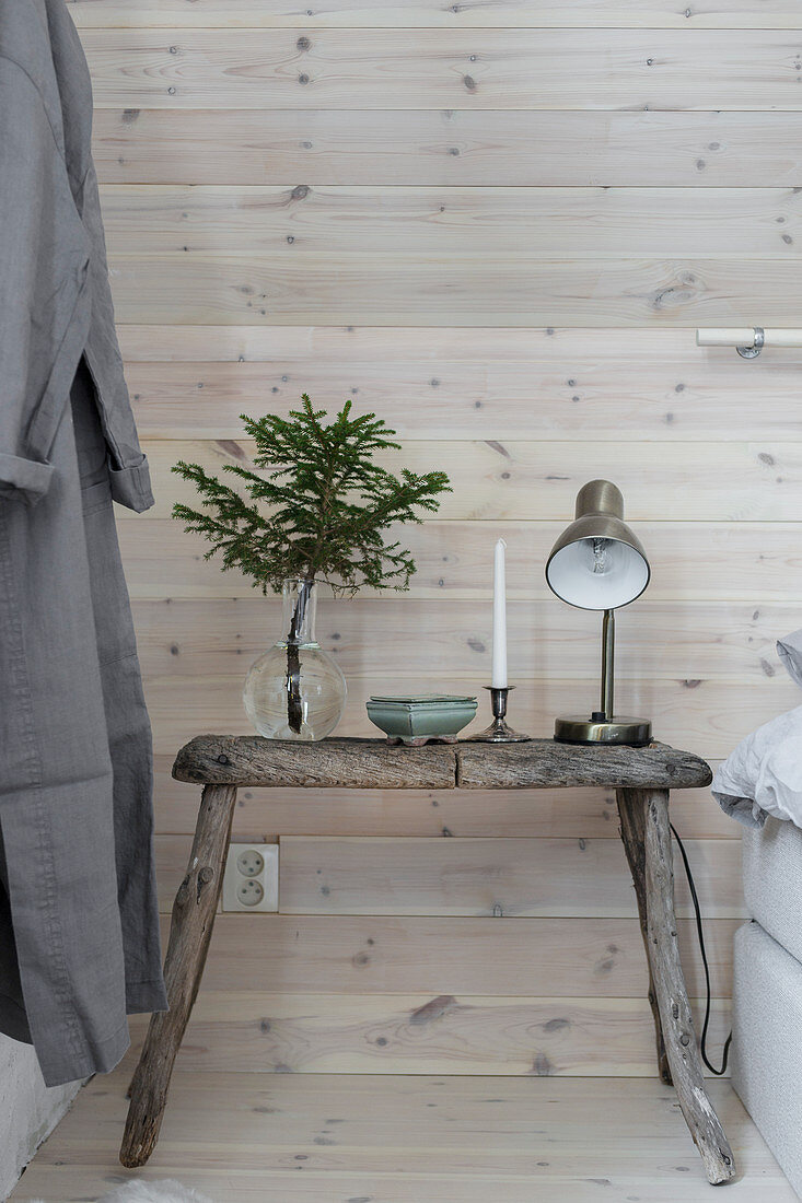 Old, weathered stool used as bedside table against board wall