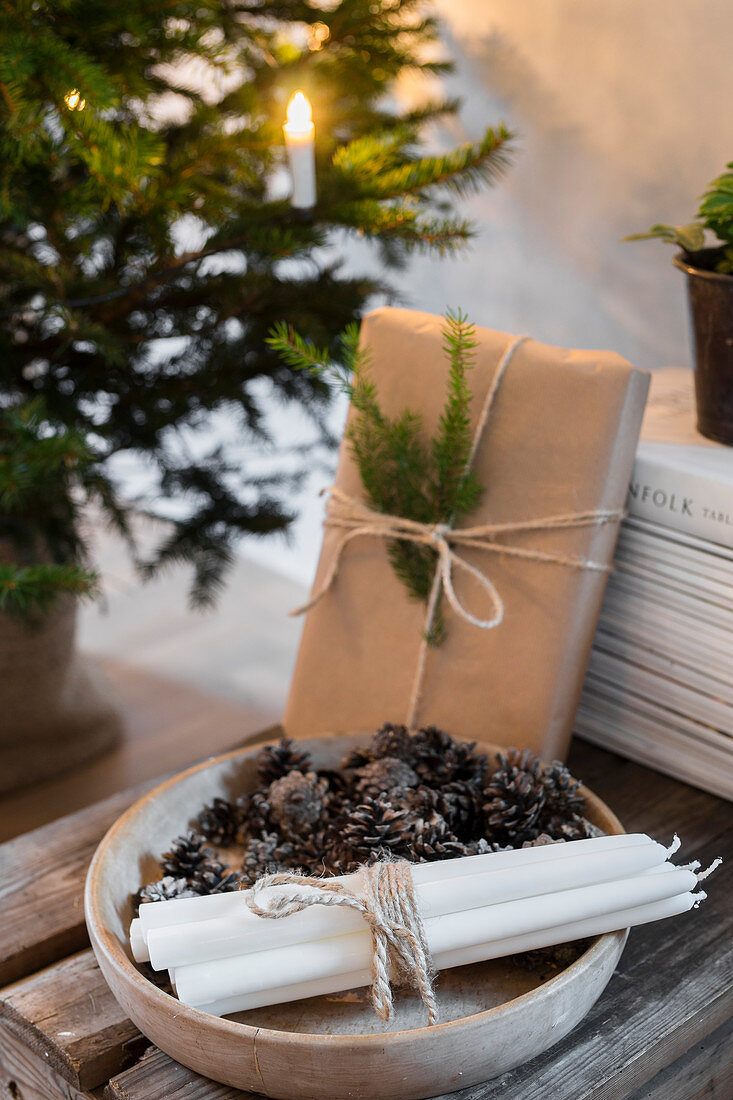 Kerzen und Zapfen in einer Holzschale und verpacktes Geschenk