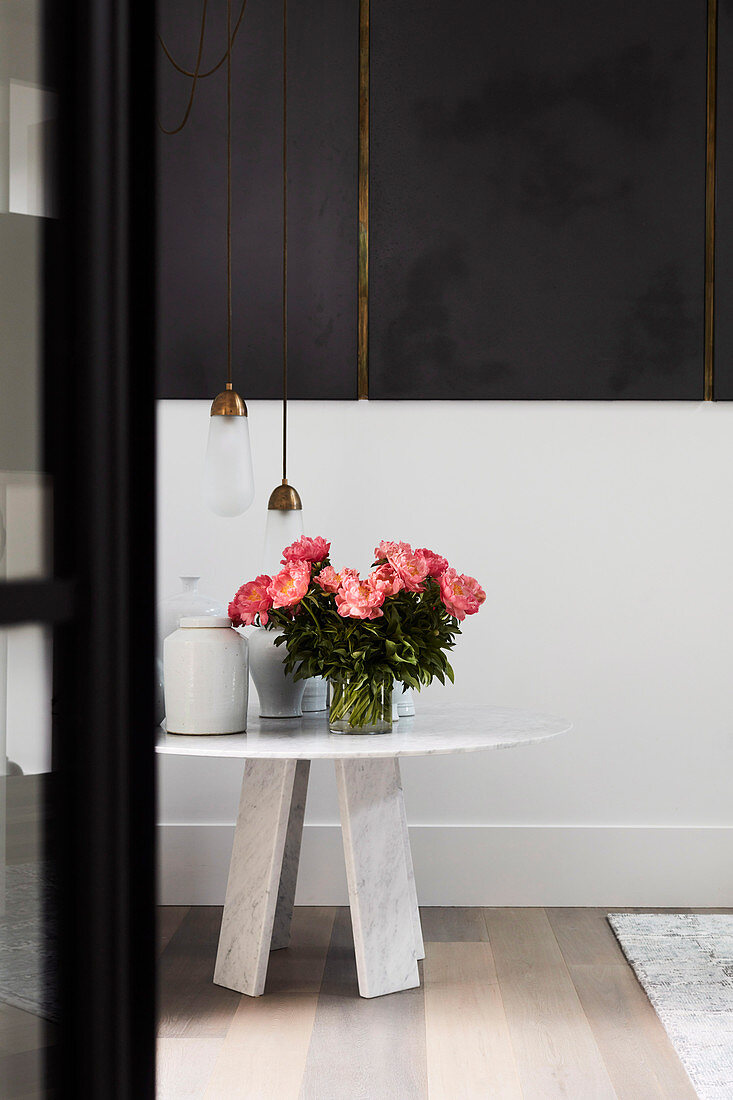 Runder Tisch mit üppigem Blumenstrauß, darüber Designerleuchte