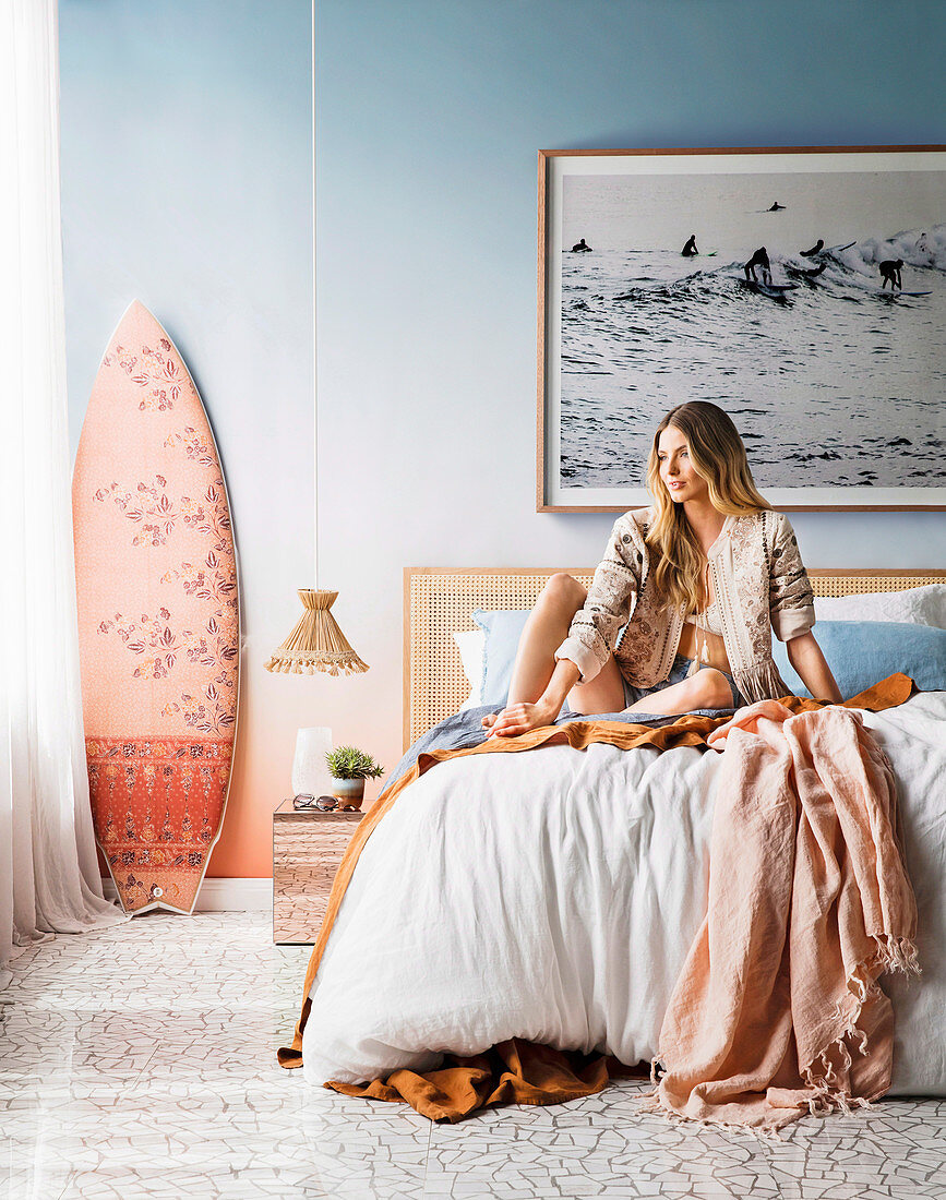 Junge Frau sitzt auf dem Bett im Schlafzimmer im Strand-Look