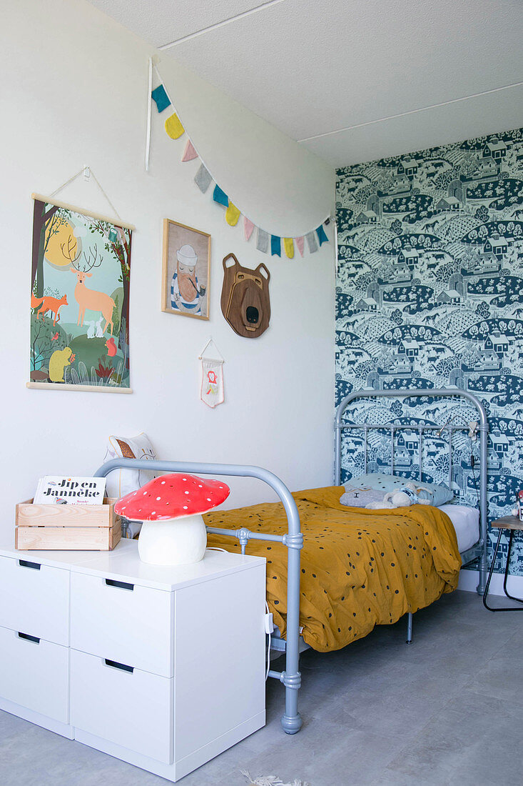 Grey metal bed against blue-patterned retro wallpaper in child's bedroom