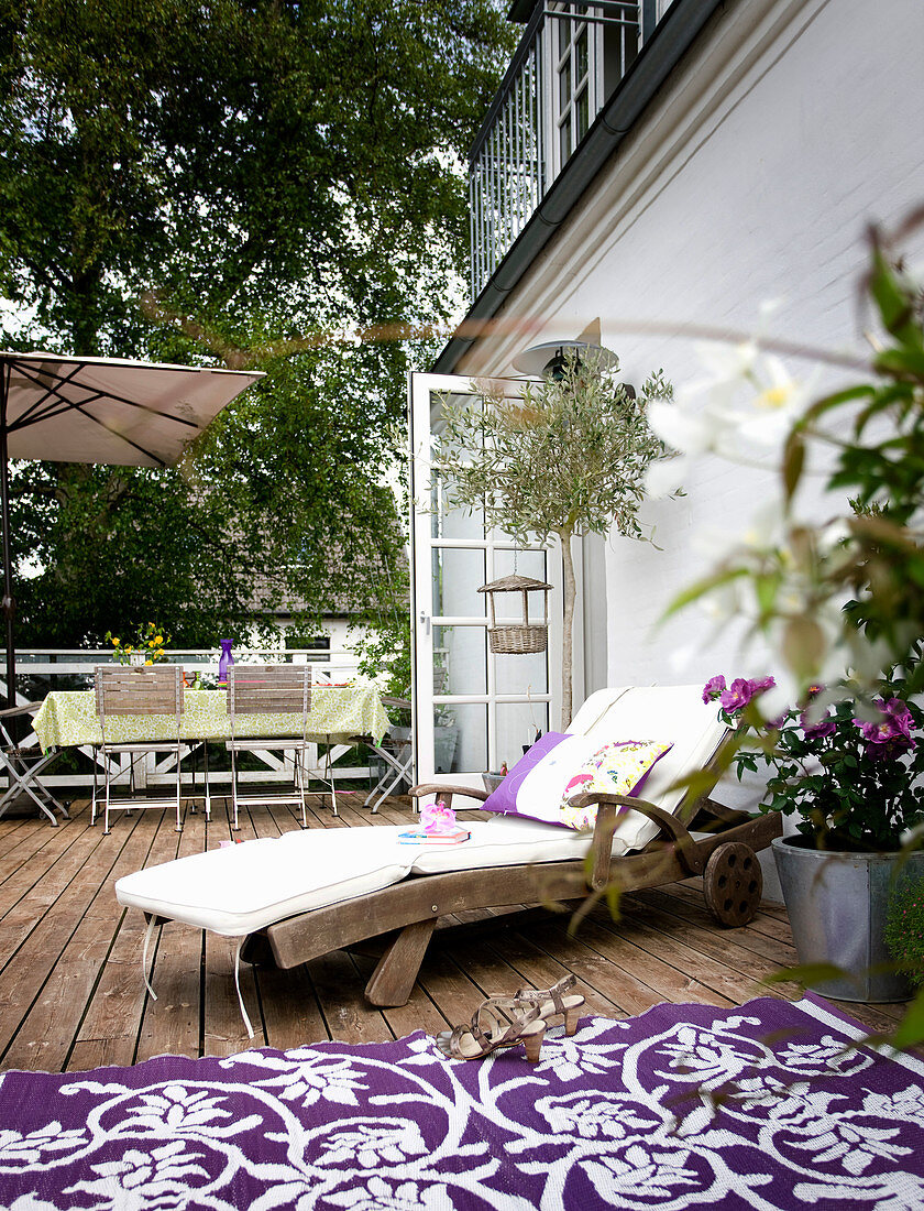 Holzliege mit Kissen und lila-weiß Teppich auf Terrasse