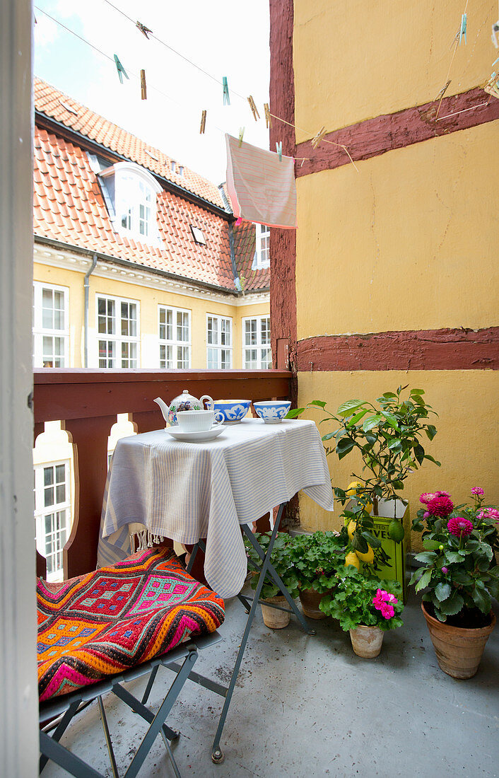 Klapptisch mit Stuhl, Topfblumen und Wäscheleine auf Balkon mit gelber Seitenwand