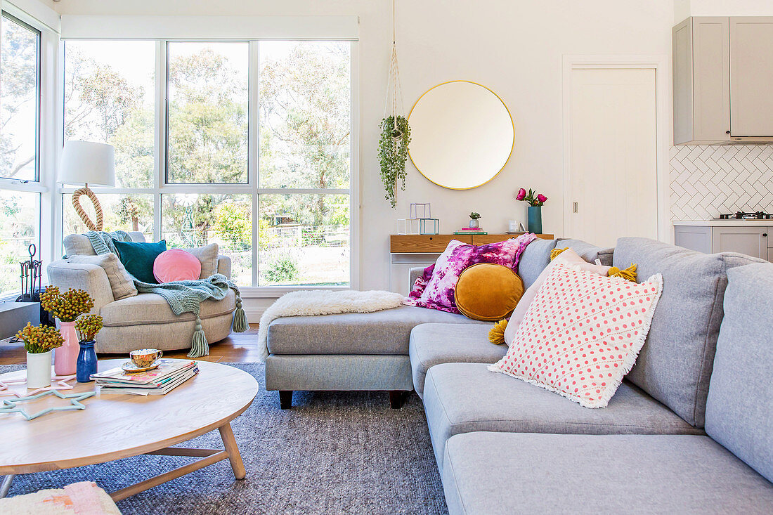 Schlichtes graues Sofa mit bunten Kissen vor der Fensterfront