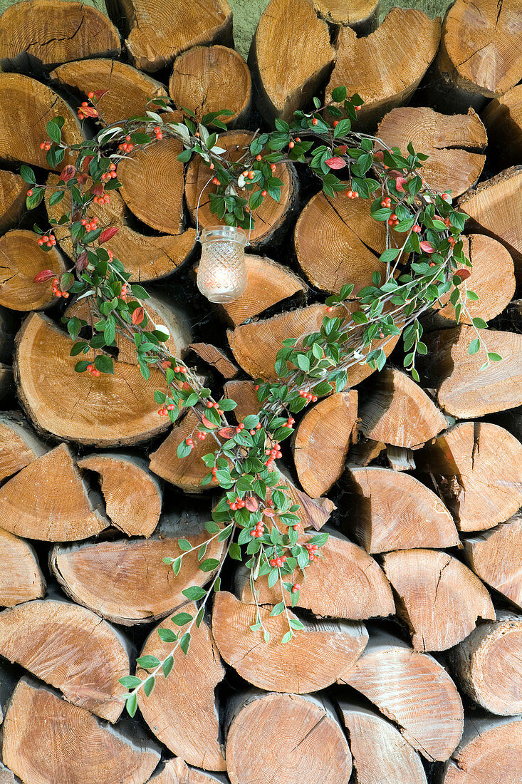 Heart-shaped wreath of cotoneaster around candle lantern on stacked firewood