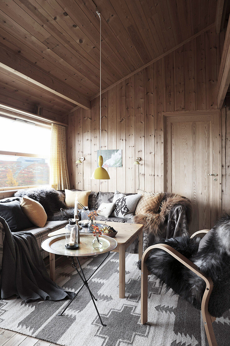 Fur blanket and cushions in seating area of wood-panelled chalet living room