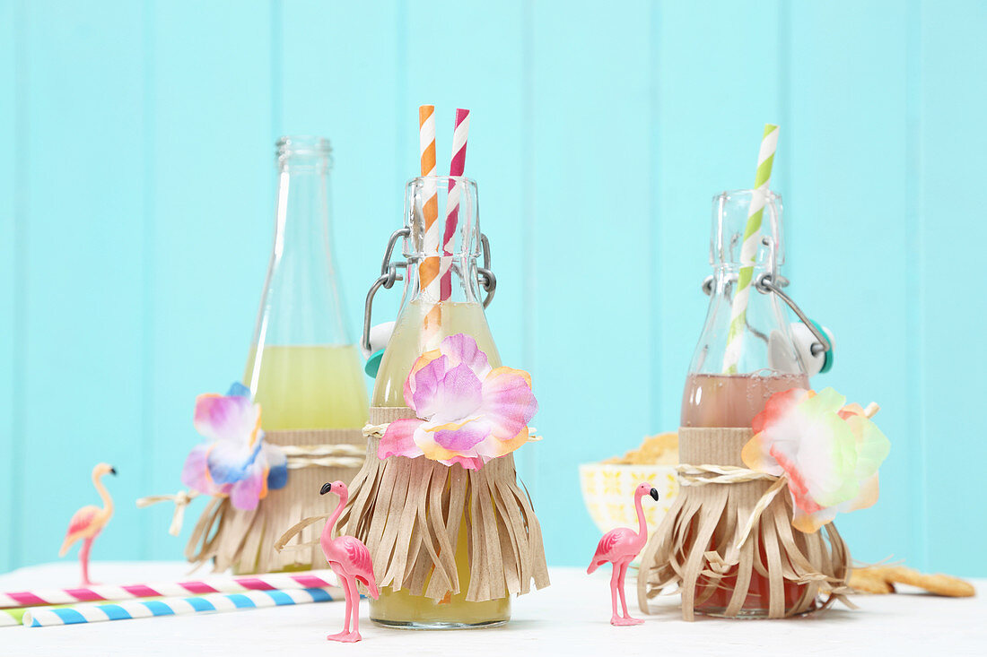 Bottles of lemonade decorated with paper strips and fabric flowers
