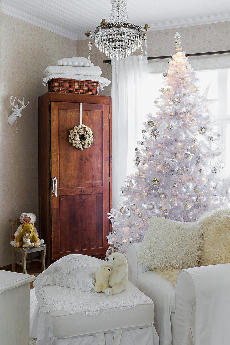 Weißer Weihnachtsbaum und weißer Hussensessel mit passendem Fußhocker vor Holzschrank