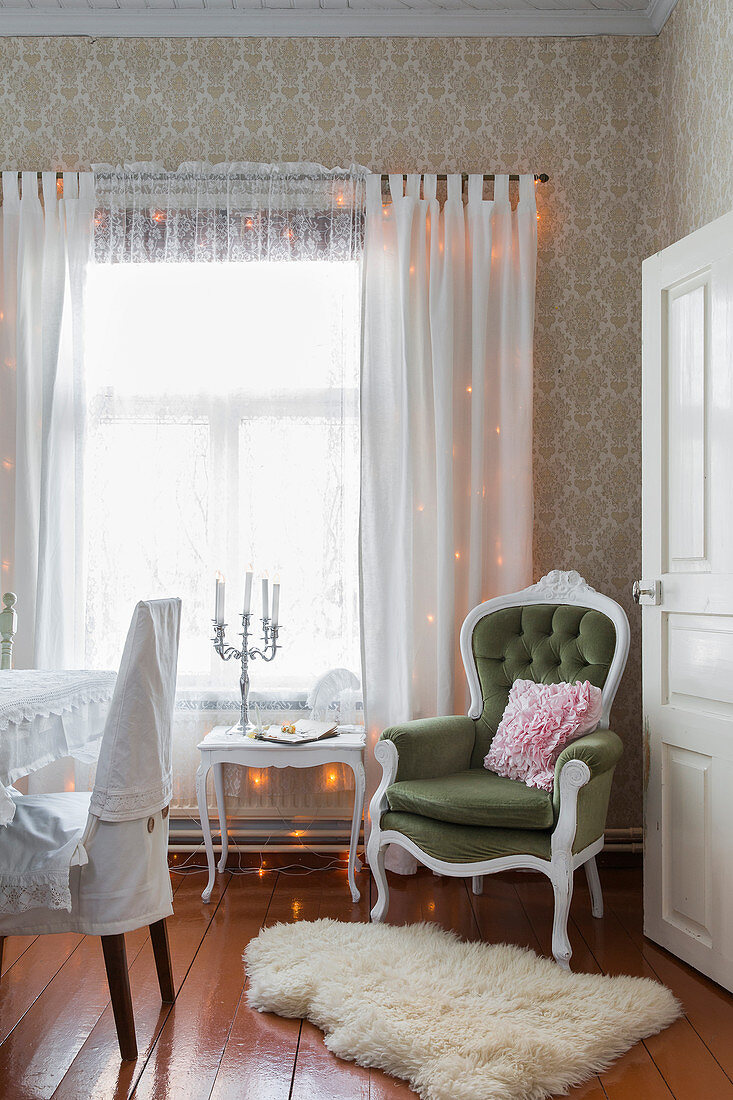 Armchair and side next to window with gauzy curtains and fairy lights