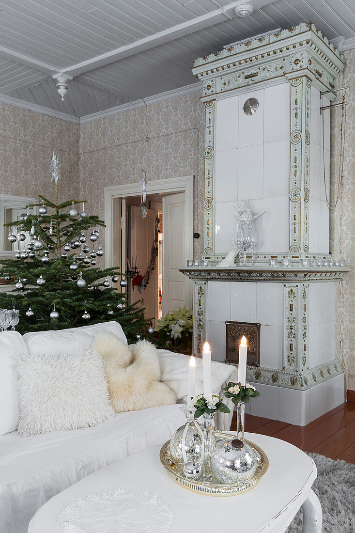 White coffee table, sofa, old tiled stove and Christmas tree in living room