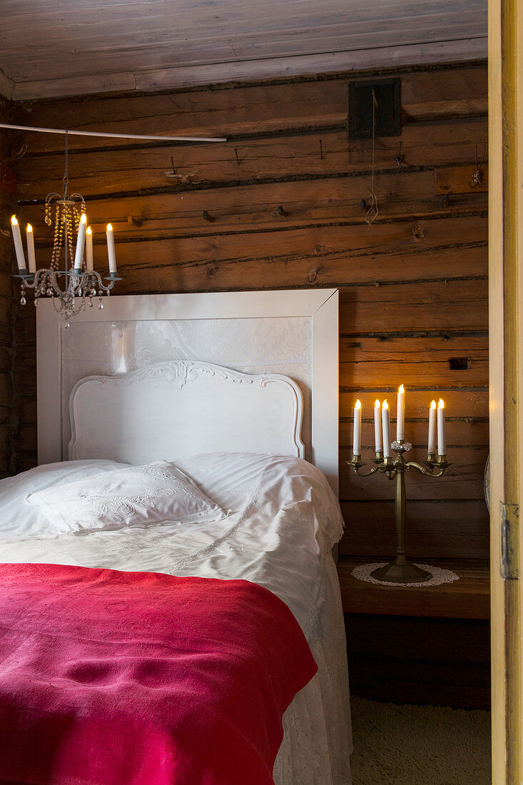 Weißes Bett und Kerzen in rustikalem Schlafzimmer mit Holzverkleidung