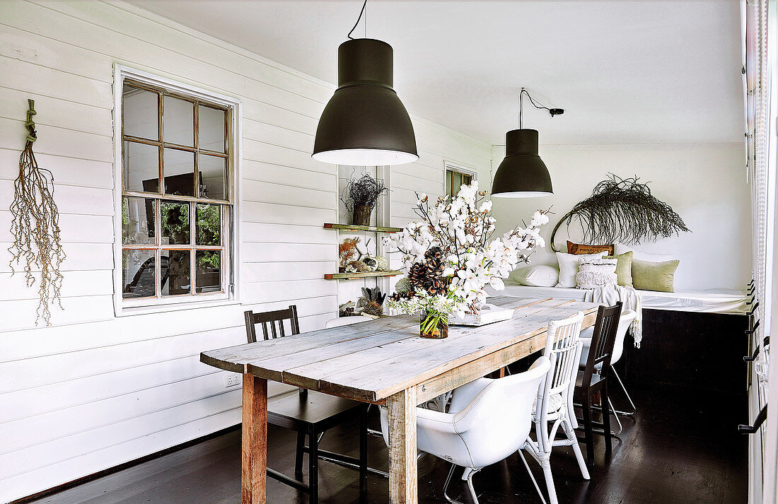 Rustic wooden table with various chairs in the dining room with white walls