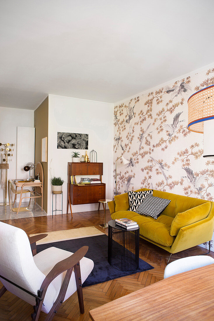Senfgelbes Sofa vor tapezierter Wand und 50er Jahre Schränkchen im Wohnzimmer