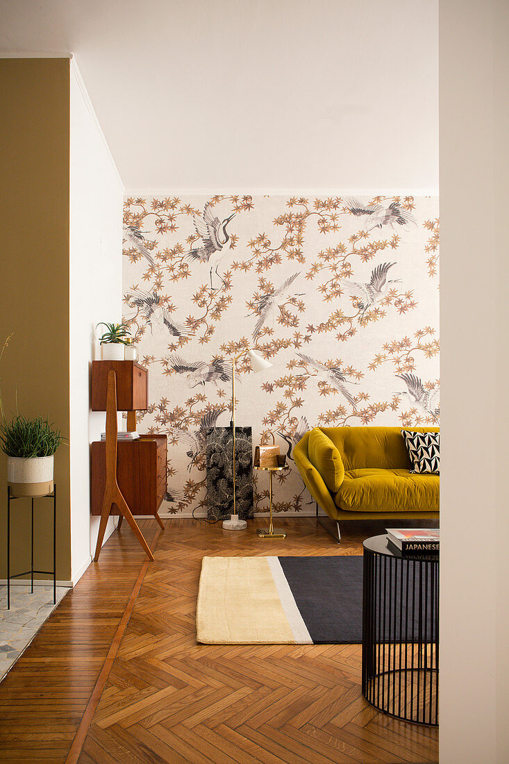 Blick ins Wohnzimmer mit senfgelbem Sofa vor tapezierter Wand und 50er Jahre Schränkchen