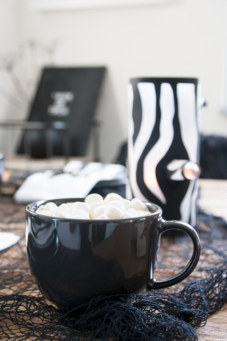 Hot drink topped with marshmallows in black cup in front of handmade tealight holder