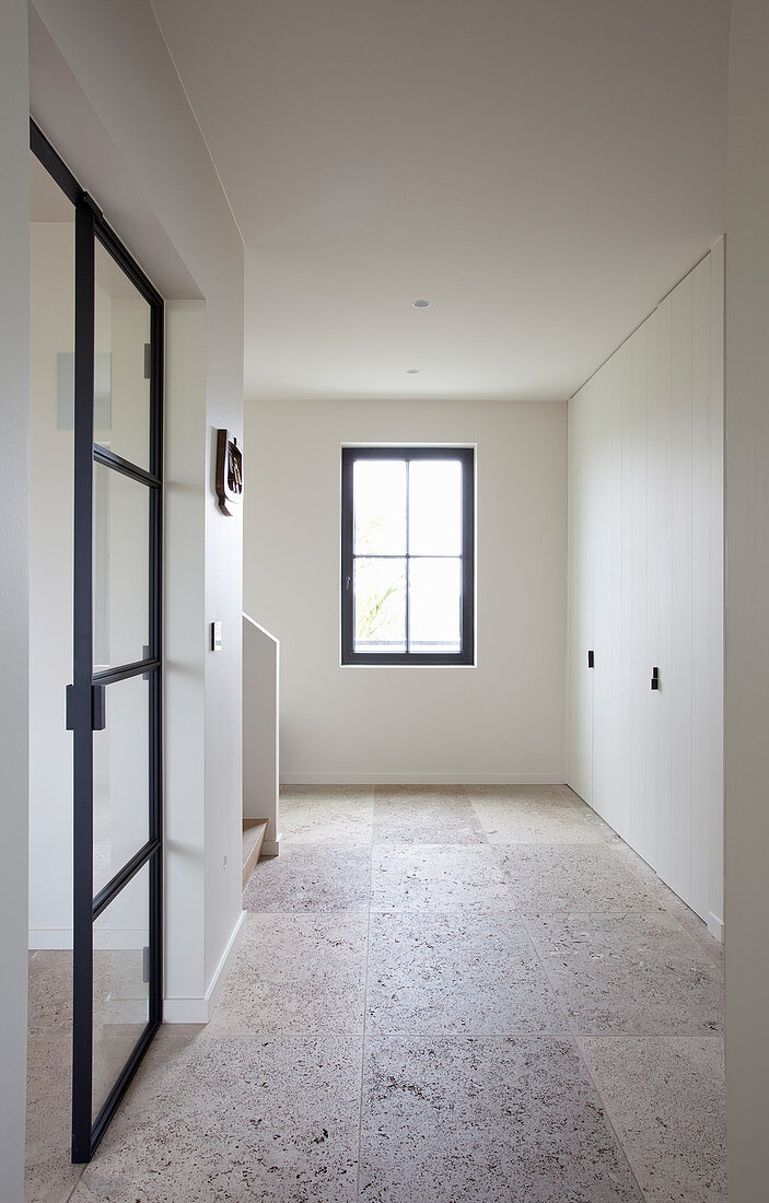 Stone-flagged floor in empty hallway with fitted white cupboards